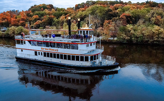 Boat from Hudson River Cruise Company navigating the river, surrounded by vibrant fall foliage.